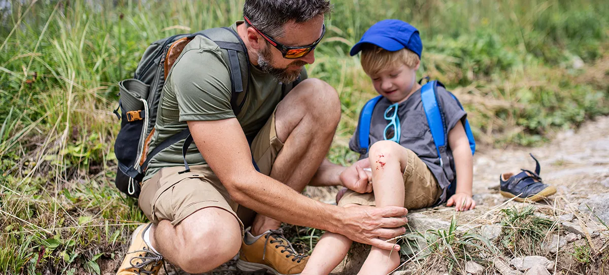 father tending to child with scraped knee on a hike