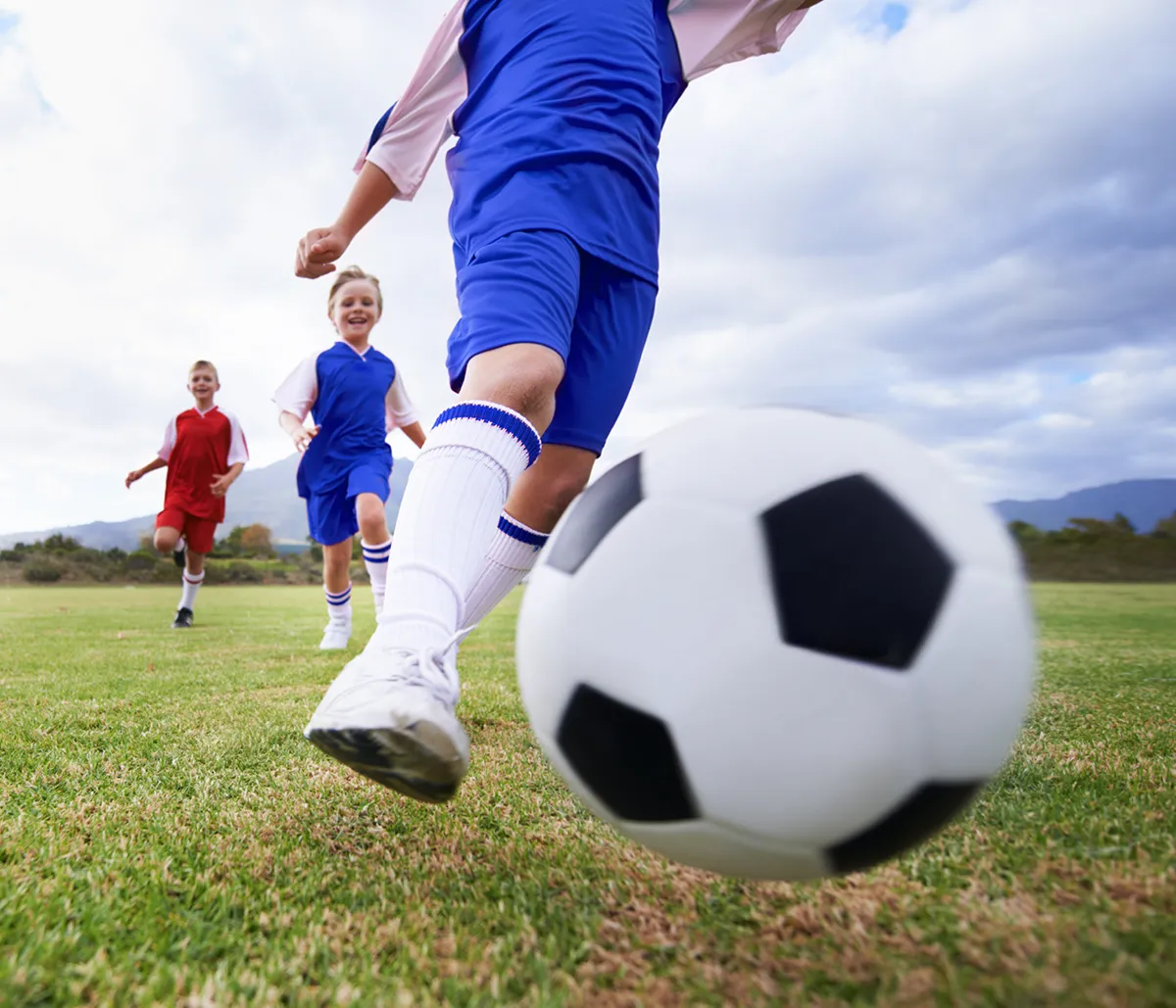 Children wearing blue jerseys running and kicking a soccer ball